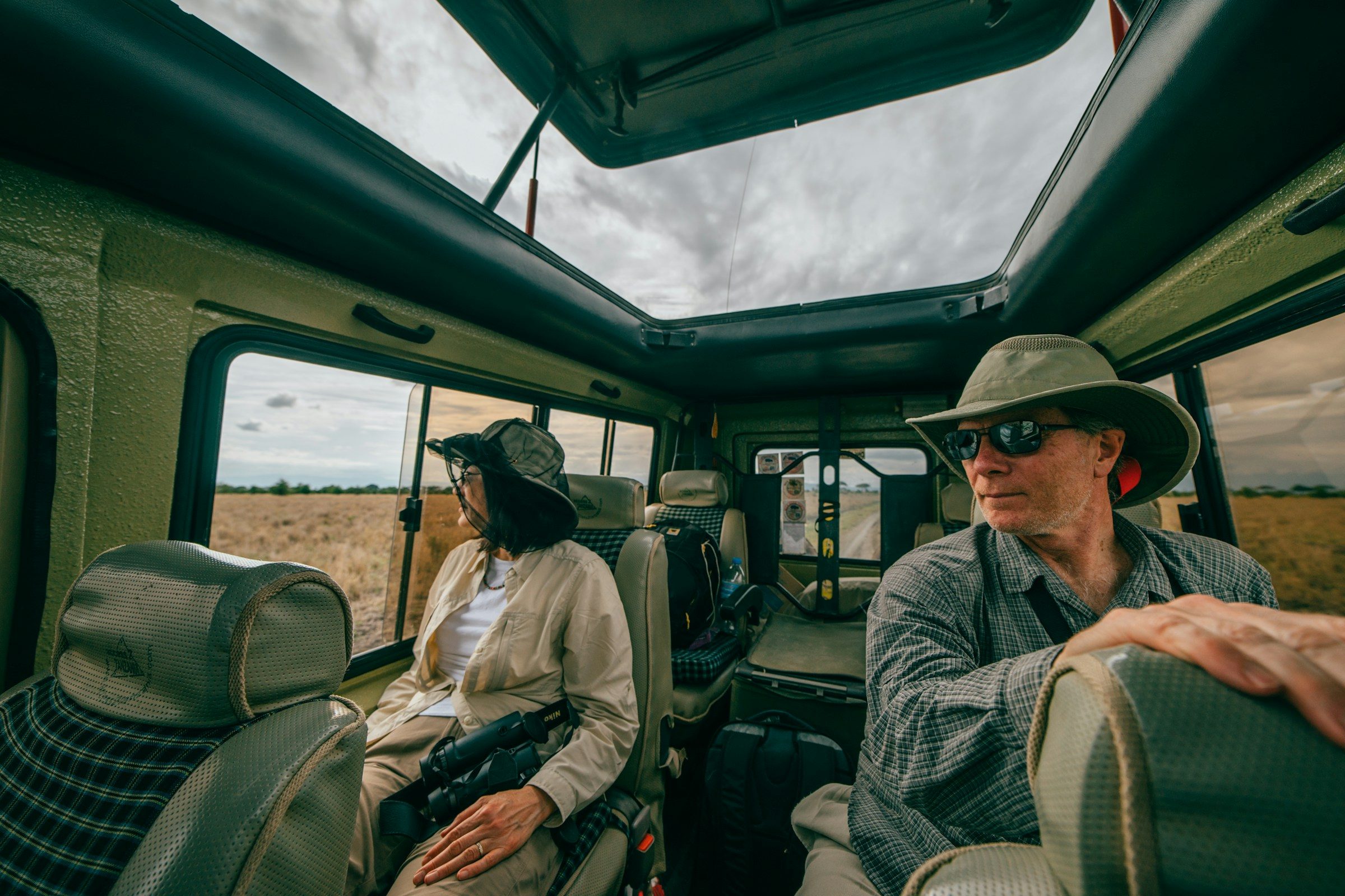 Two travellers seated inside a safari vehicle with the roof raised, Tanzania